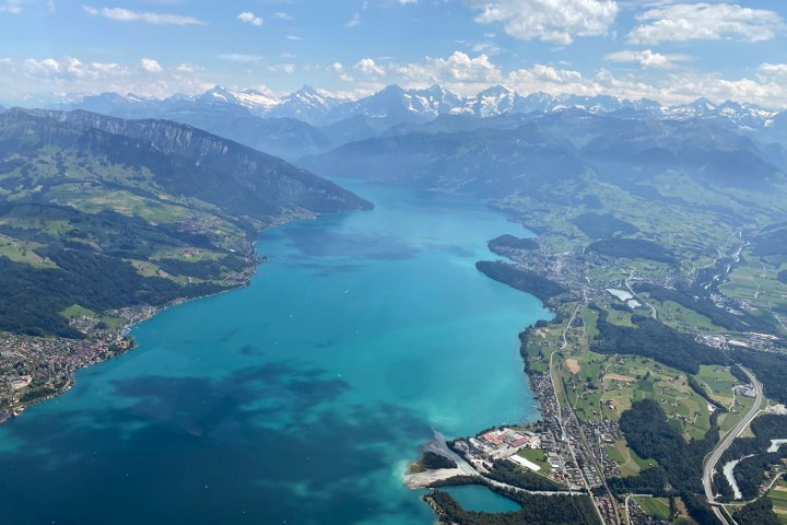 Aerial view of a turquoise lake surrounded by mountains and green landscapes under a blue sky with clouds.