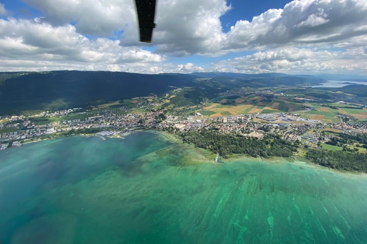 Aerial view of a lakeside town with green water, fields, and cloudy sky.