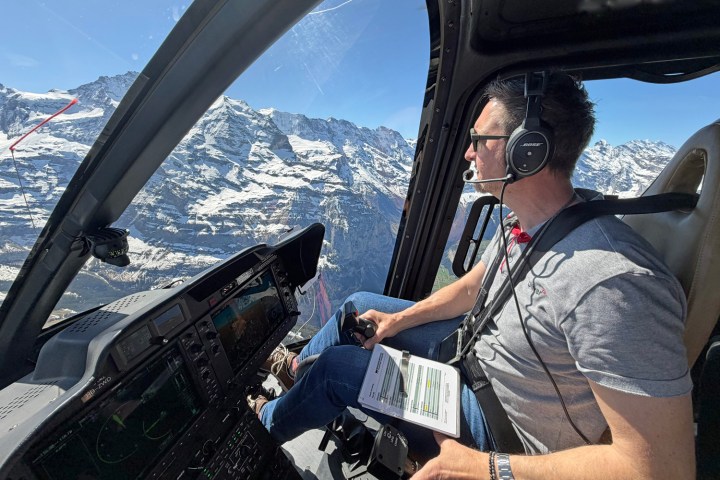 Pilot controlling helicopter from cockpit with Swiss Alps visible outside during a scenic flight.
