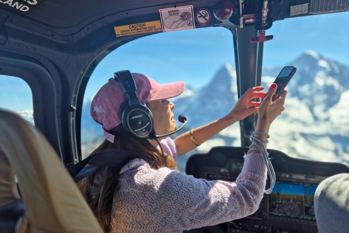 Passenger wearing comfortable clothing and an aviation headset while taking photos of the Swiss Alps from inside a Bell 505 helicopter during a private FunFlights scenic flight.