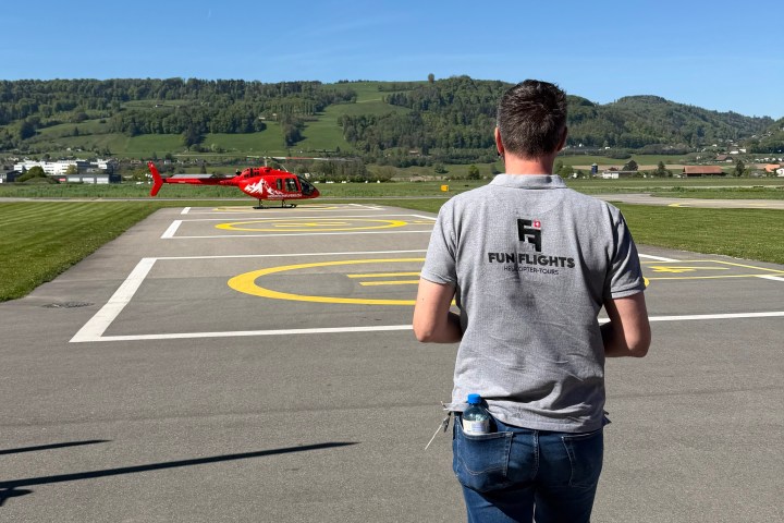 FunFlights chief pilot walking from the hangar towards a red Bell 505 helicopter parked on the airport tarmac.